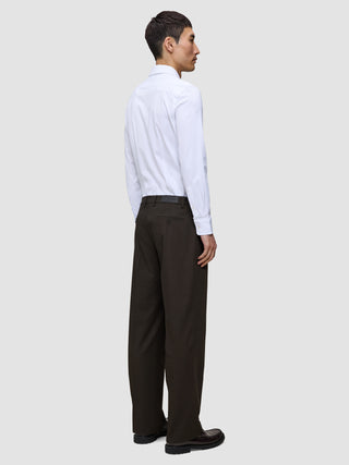 Eine Person in einem weißen Hemd und einer Motion Suit-Hose Relaxed Cognac, im Profil stehend.