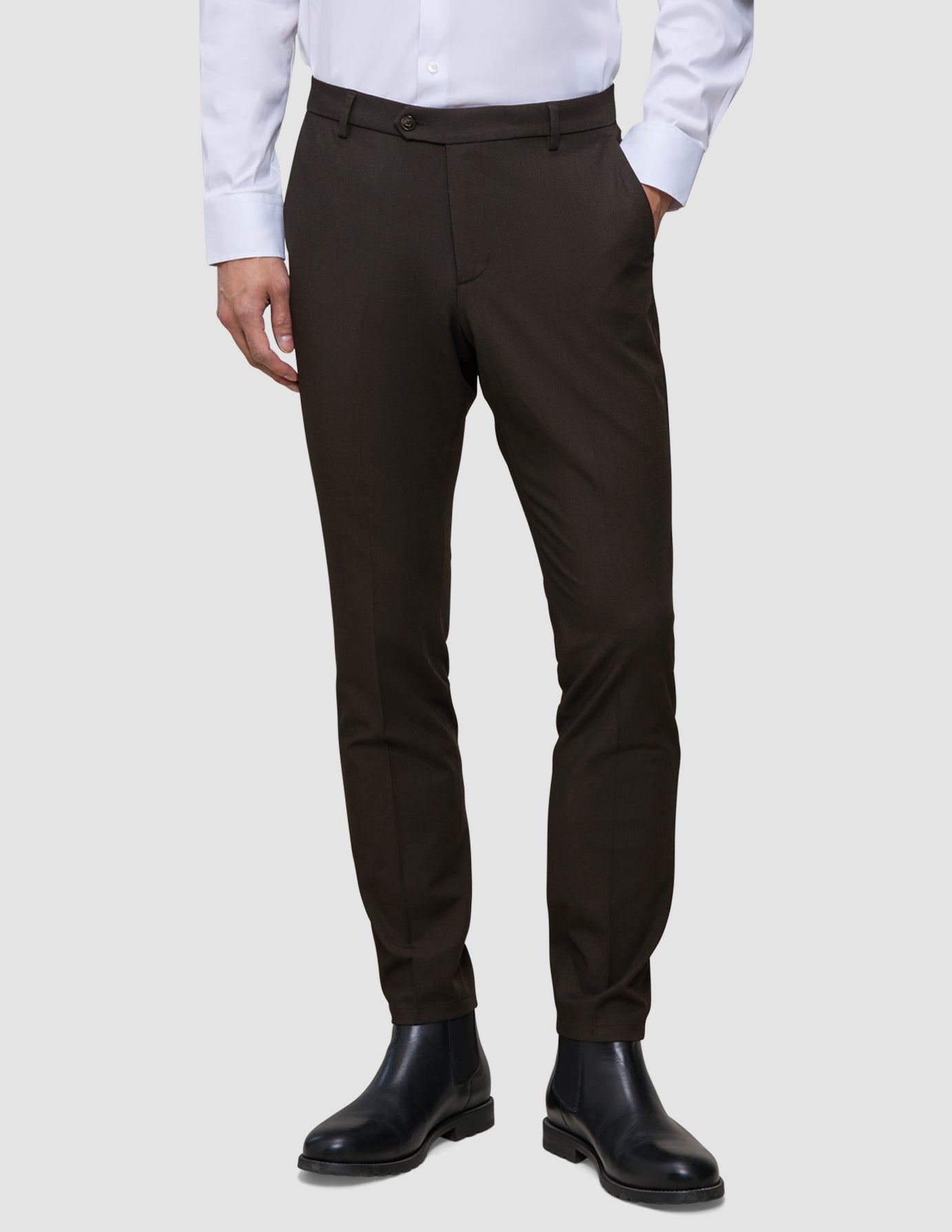Eine Person, die ein weißes Hemd, eine schmal geschnittene, cognacfarbene Motion-Anzughose und schwarze Chelsea-Stiefel aus Leder trägt und damit einen eleganten Look präsentiert.