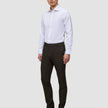 Ein Mann in einem weißen Hemd und einer schmal geschnittenen Motion Suit-Hose in der Farbe Slim Cognac, kombiniert mit schwarzen Lederstiefeln für einen eleganten Look.