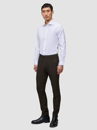 Ein Mann in einem weißen Hemd und einer schmal geschnittenen Motion Suit-Hose in der Farbe Slim Cognac, kombiniert mit schwarzen Lederstiefeln für einen eleganten Look.