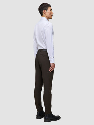 Ein Mann steht im Profil da und trägt ein weißes Hemd sowie eine Motion Suit Pants Slim Cognac – ein eleganter Look.