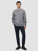 Ein Mann, der einen grauen Pullover mit Rundhalsausschnitt über einem weißen Hemd mit Kragen trägt, dazu eine Motion-Anzughose in der Farbe Slim Midnight Blue und braune Slipper.