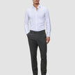 Ein Mann, der ein weißes Hemd, eine Motion Suit-Hose in der Farbe Slim Pepper Grey und schwarze Slipper trägt.
