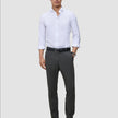 Ein Mann, der ein weißes Hemd, einen schwarzen Gürtel, eine Motion Suit-Hose in der Farbe Slim Pepper Grey und schwarze Slipper trägt.