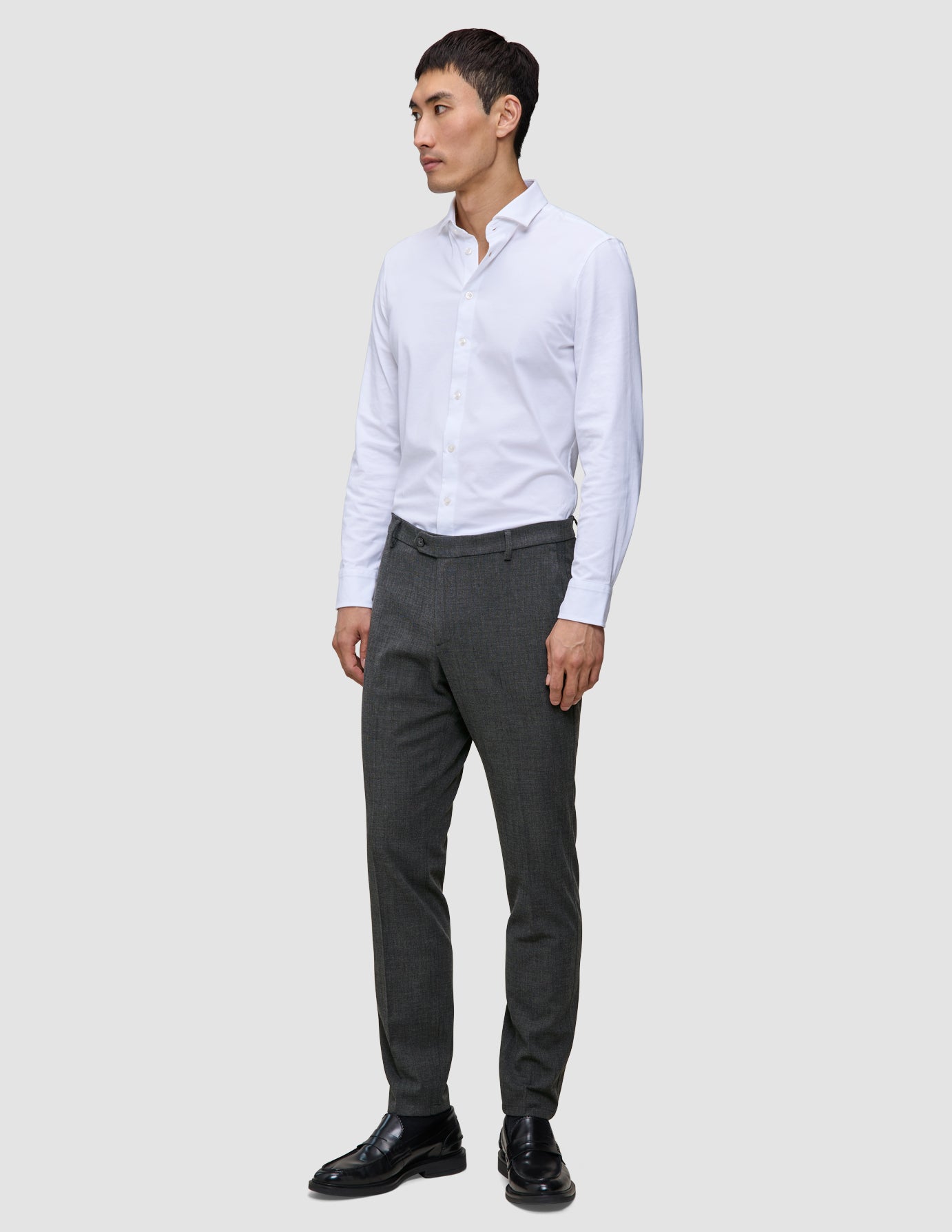 Ein Mann, der ein weißes Hemd, eine Motion Suit-Hose in der Farbe Slim Pepper Grey und schwarze Anzugschuhe trägt.