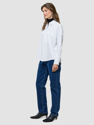 Eine Frau, die ein weißes, übergroßes Langarmshirt, eine dunkle Jeans und schwarze Stiefel mit Absatz trägt.