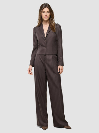 Eine Frau trägt den „Women Raina Short Blazer Chestnut Pinstripe“ und eine dazu passende Hose mit weitem Bein – ein eleganter Look.