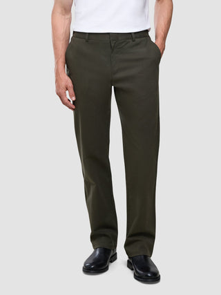 Ein Mann, der eine „Refine Cotton Pants Relaxed Fit Dark Olive“ und ein weißes Hemd trägt.