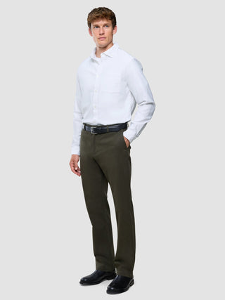 Ein Mann, der ein weißes, langärmeliges Hemd mit Knöpfen, eine „Refine Cotton Pants Relaxed Fit“ in Dunkeloliv sowie einen schwarzen Gürtel und schwarze Schuhe trägt.
