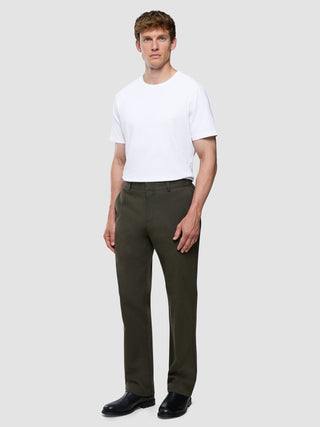 Ein Mann, der ein weißes T-Shirt, eine „Refine Cotton Pants Relaxed Fit Dark Olive“ und schwarze Schuhe trägt.