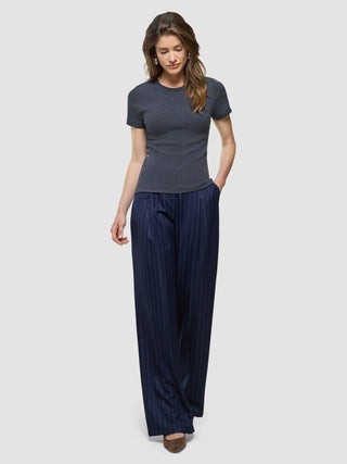 Eine Frau, die ein „Women Rib“-T-Shirt in Dunkelgrau-Melange und eine marineblaue Hose mit weitem Bein und Nadelstreifen trägt.