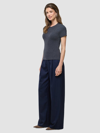 Eine Frau, die ein „Women Rib“-T-Shirt in Dunkelgrau-Melange und eine marineblaue Hose mit Nadelstreifen und weitem Bein trägt.