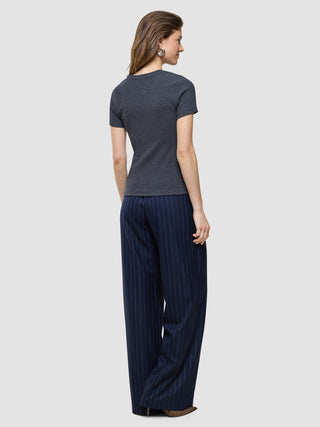 Eine Frau, von hinten gesehen, die ein „Women Rib“-T-Shirt in Dunkelgrau-Melange und eine marineblaue, breit geschnittene Hose mit Nadelstreifen trägt.