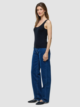 Eine Frau im Profil, die ein schwarzes Rib-Tanktop und eine blaue Jeans trägt.