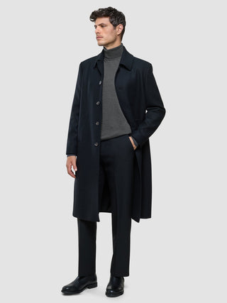 Ein Mann, der unter einem dunklen Mantel einen nahtlosen Premium-Merino-Strickpullover mit Rollkragen in Anthrazit trägt, dazu eine schwarze Hose und Stiefel.