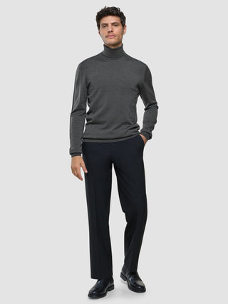Ein Mann, der einen nahtlosen Premium-Merino-Rollkragenpullover in Anthrazit, eine schwarze Hose und schwarze Schuhe trägt.