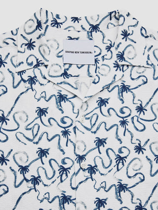 Ein kurzärmeliges Seersucker-Hemd in Marineblau mit Palmenmotiv, weißem Hintergrund und einem blauen, handgezeichneten Palmen- und Schnörkelmuster in moderner Passform.