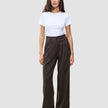Eine Person, die ein weißes T-Shirt und eine weit geschnittene Serene Pants Wide Walnut Herringbone mit vertikalen Nadelstreifen trägt.