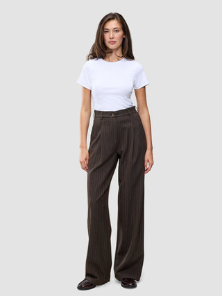 Eine Person, die ein weißes T-Shirt und eine weit geschnittene Serene Pants Wide Walnut Herringbone mit vertikalen Nadelstreifen trägt.