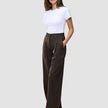 Eine Frau, die ein weißes T-Shirt und die Serene Pants Wide Walnut Herringbone trägt, die sich durch ein dezentes vertikales Streifenmuster und einen weiten Schnitt im skandinavischen Stil auszeichnen.