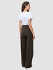 Eine Frau, von hinten gesehen, trägt ein weißes T-Shirt und eine braune Serene Pants Wide Walnut Herringbone mit weitem Bein und dezentem vertikalem Nadelstreifenmuster, die das minimalistische skandinavische Design verkörpert.