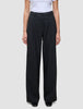 Eine Person, die eine hoch taillierte schwarze Serene Pants Wide Black mit weitem Bein und Falten auf der Vorderseite trägt, dazu ein weißes, in die Hose gestecktes T-Shirt.