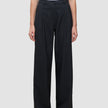 Eine Person, die eine hoch taillierte schwarze Serene Pants Wide Black mit weitem Bein und Falten auf der Vorderseite trägt, dazu ein weißes, in die Hose gestecktes T-Shirt.