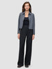 Eine Frau, die eine graue Jacke mit Reißverschluss, ein schwarzes Trägertop und eine schwarze Hose mit weitem Bein vom Modell Serene Pants Wide Black trägt.