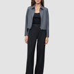 Eine Frau, die eine graue Jacke mit Reißverschluss, ein schwarzes Trägertop und eine schwarze Hose mit weitem Bein vom Modell Serene Pants Wide Black trägt.