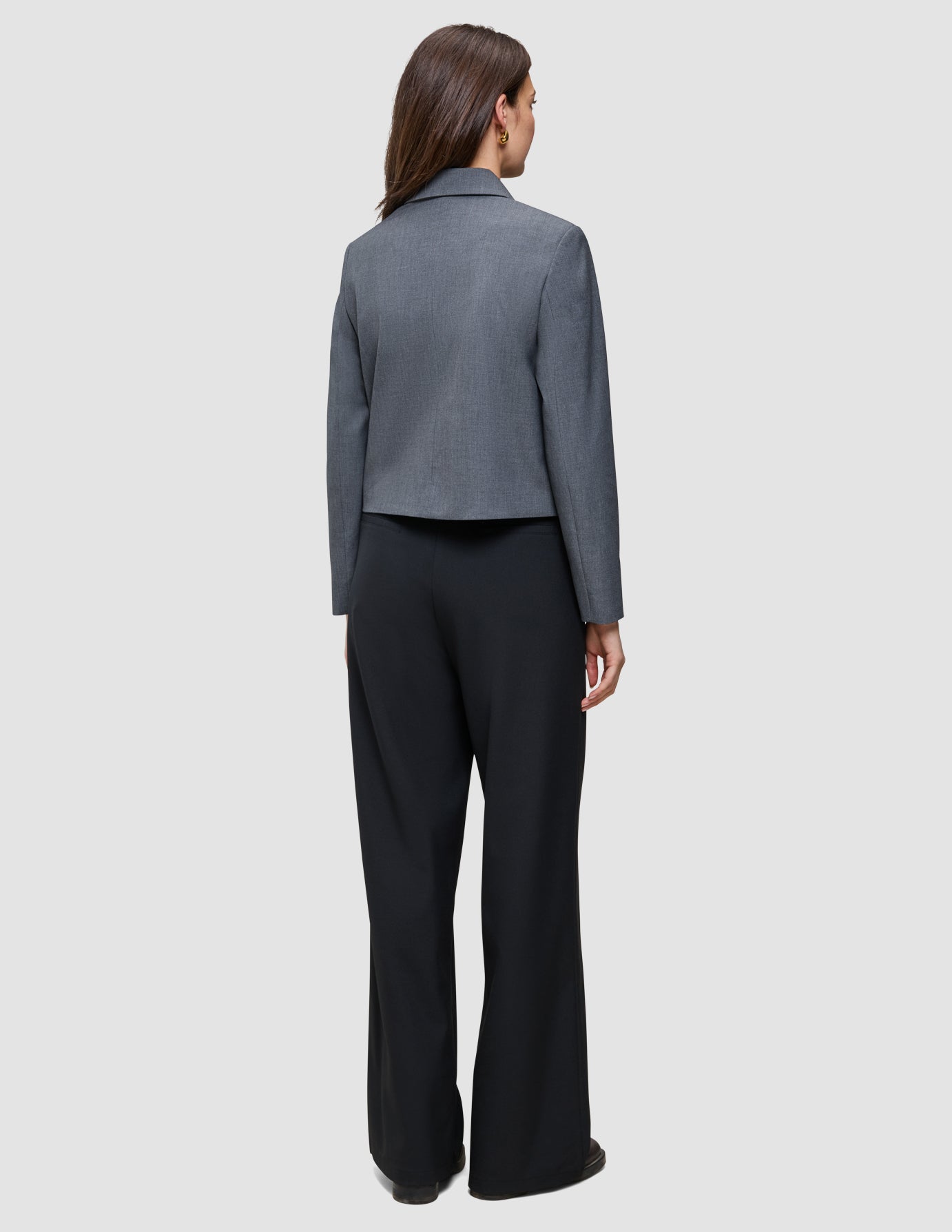 Eine Frau, von hinten gesehen, die einen grauen Blazer und eine schwarze Serene Pants Wide Black mit weitem Bein trägt.