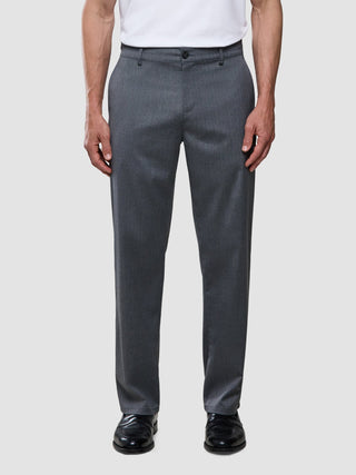 Ein Mann, der ein weißes T-Shirt, eine Siena-Hose in Relaxed-Fit mit Fischgrätenmuster in Grau und schwarze Anzugschuhe trägt.