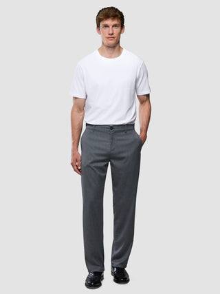 Ein Mann, der steht und ein weißes T-Shirt, eine „Siena“-Hose in lockerer Passform mit Fischgrätenmuster in Grau sowie schwarze Anzugschuhe trägt.
