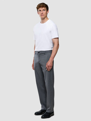 Ein Mann, der ein weißes T-Shirt mit Rundhalsausschnitt und eine „Siena Pants Relaxed Fit Herringbone Grey“ trägt, dazu schwarze Anzugschuhe.