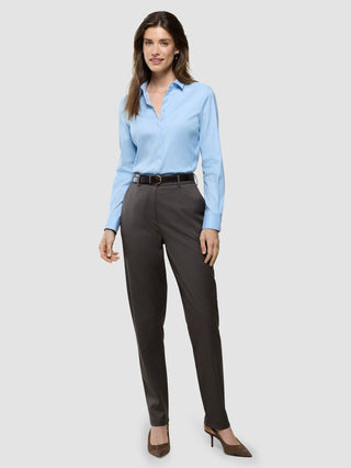 Eine lächelnde Frau, die ein hellblaues Hemd trägt, das in die „Women Skye Pants Tapered Dark Chestnut Melange“ gesteckt ist, dazu einen Gürtel und braune Pumps.