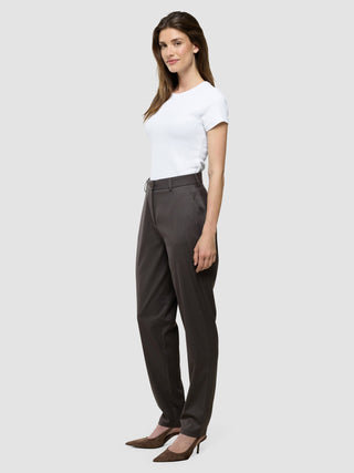 Eine Frau, die ein weißes T-Shirt und eine „Women Skye Pants Tapered Dark Chestnut Melange“ trägt, steht seitlich.