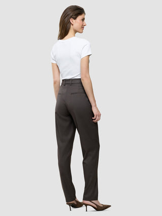 Eine Frau im Profil trägt ein weißes T-Shirt, die „Women Skye Pants Tapered Dark Chestnut Melange“ und Pumps mit spitzer Zehenpartie.