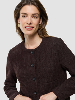 Eine Frau, die eine kurze Damenjacke „Sorae“ in der Farbe „Espresso“ und runde goldene Ohrringe trägt.