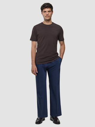 Ein Mann trägt ein Supima-T-Shirt in der Farbe „Deep Brown“ zu einer blauen Hose und dunklen Schuhen, die alle durch ein minimalistisches skandinavisches Design bestechend sind.