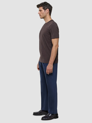 Ein Mann im Profil, der ein Supima-T-Shirt in Deep Brown, eine marineblaue Hose mit 360°-Stretch und schwarze Slipper trägt.