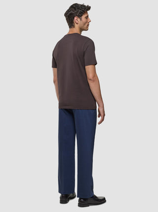 Ein Mann, von hinten gesehen, der ein Supima-T-Shirt in der Farbe „Deep Brown“, eine blaue Hose und dunkle Slipper mit 360°-Stretch trägt.