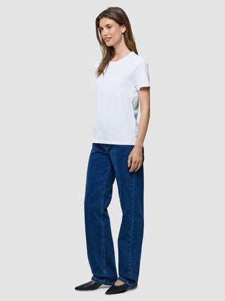 Eine Frau, die ein weißes Supima-T-Shirt, eine blaue Jeans und schwarze Schuhe mit spitzer Zehenpartie trägt.