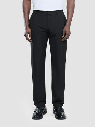 Ein Mann, der ein weißes T-Shirt, eine schwarze „Tech Linen Elastic“-Hose und schwarze Slipper trägt.
