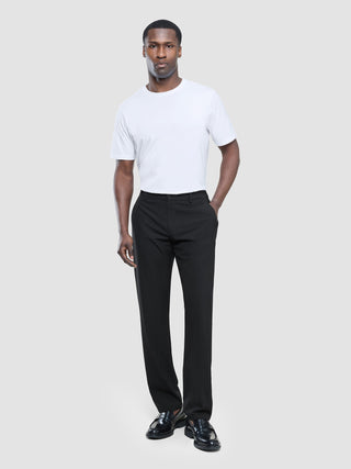 Ein Mann, der ein weißes T-Shirt mit Rundhalsausschnitt, eine schwarze „Tech Linen Elastic“-Hose und schwarze Slipper trägt.