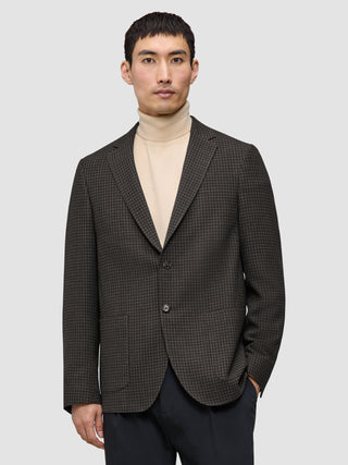 Ein Mann, der einen dunkelbraunen, karierten Timeless Wool Blazer Slim über einem beigen Rollkragenpullover trägt.