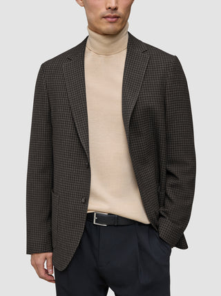 Eine Person, die einen dunkelbraunen, karierten Timeless Wool Blazer Slim über einem beigen Rollkragenpullover und einer schwarzen Hose trägt.