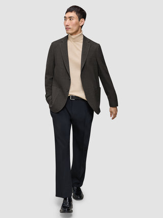 Ein Mann, der einen dunkelbraunen, karierten Timeless Wool Blazer Slim über einem hellbraunen Rollkragenpullover, einer dunklen Hose und schwarzen Loafern trägt.