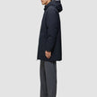 Seitenansicht einer Person, die eine schwarze Utility-Jacke trägt: schwarze Jacke aus recyceltem Polyester, graue Hose und schwarze Schuhe.