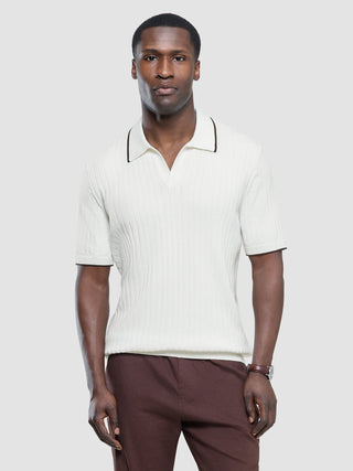 Ein Mann, der ein weißes, kurzärmeliges Polohemd mit V-Ausschnitt und braunem Kragenbesatz sowie eine braune Hose trägt.