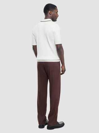 Ein Mann, von hinten gesehen, der ein weißes, kurzärmeliges Polohemd mit V-Ausschnitt und braunem Kragen sowie eine braune Hose trägt.