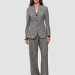 Eine Frau trägt einen grauen, strukturierten Women Ashryn Pants Wide Domino Herringbone-Anzug aus Bouclé-Stoff mit Fischgrätenmuster, bestehend aus einem Blazer mit drei Knöpfen und einer hoch taillierten Hose mit weitem Bein.